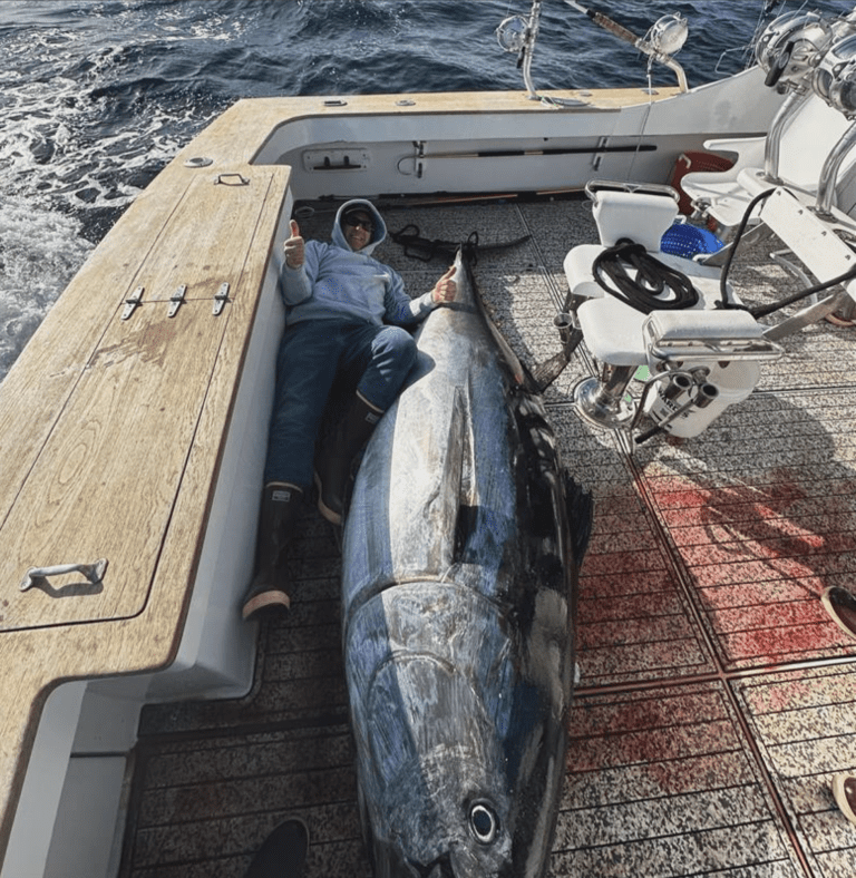 Guy laying on baot dek with a tuna he just caught while fishing